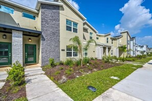 A row of modern townhouses with stone accents, green doors, and a well-maintained lawn.