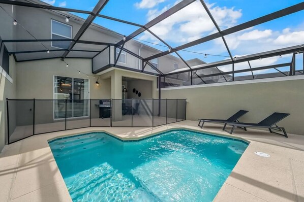 An indoor swimming pool with a glass ceiling, surrounded by lounge chairs and a covered patio area.