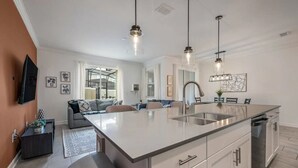 Een moderne keuken met een groot eiland, roestvrijstalen apparatuur en hangende lampen.