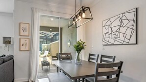 Een moderne eetruimte met een rechthoekige tafel, vier stoelen, een bankje en een hanglamp. Er zijn kunstwerken in lijsten aan de muur en een potplant op de tafel.