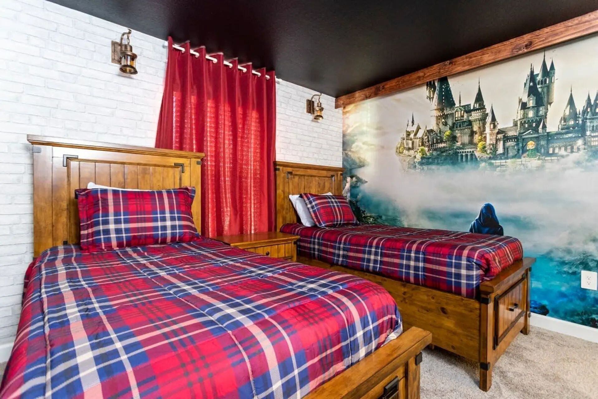 Een slaapkamer met twee houten bedden, rode gordijnen en een muurschildering van een kasteel.