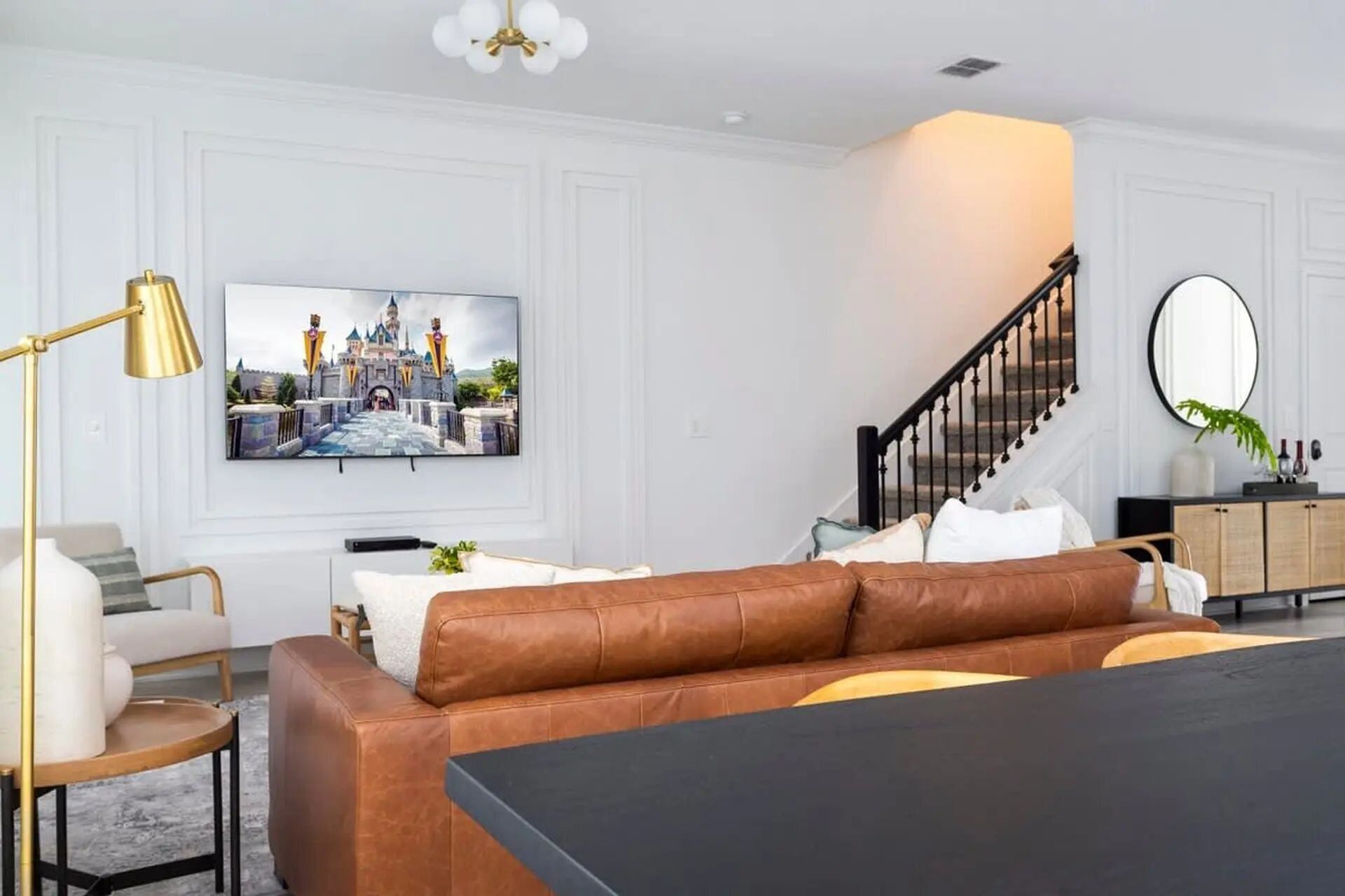 Una sala de estar moderna con un sofá de cuero marrón, una mesa de centro negra y un televisor de pared mostrando un castillo.
