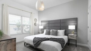 A modern bedroom with a large bed, two bedside tables, a dark headboard, and a window with blinds. - Storey Lake 4BR Townhome w/ Private Pool (Kissimmee)