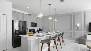 A modern kitchen with a central island, stainless steel appliances, pendant lighting, and a bar area with stools. - Storey Lake 4BR Townhome w/ Private Pool (Kissimmee)