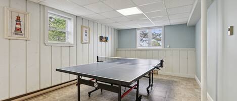 A ping pong table in a room with white paneled walls, two windows, and a ceiling with square tiles.
