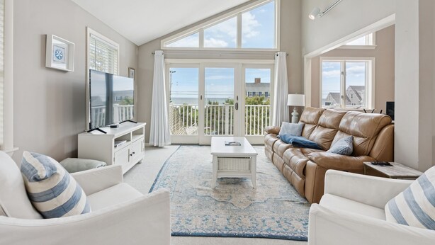 A spacious living room with a large window, a leather sofa, a white coffee table, and a TV on a white cabinet. - Drakes Island! Ocean Views!- Across from Drake's Island Beach! (Wells)