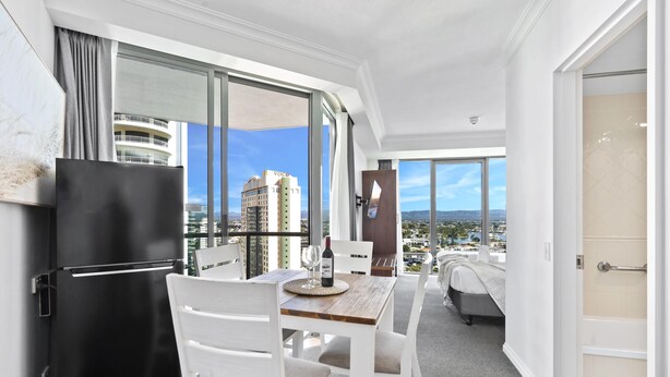 A modern hotel room with a balcony, a dining area, and a view of the cityscape. - Comfortable Standard Studio in Surfers Paradise (Surfers Paradise)