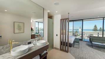 A modern bathroom with a large mirror, two sinks, and a view of the sea through large windows.