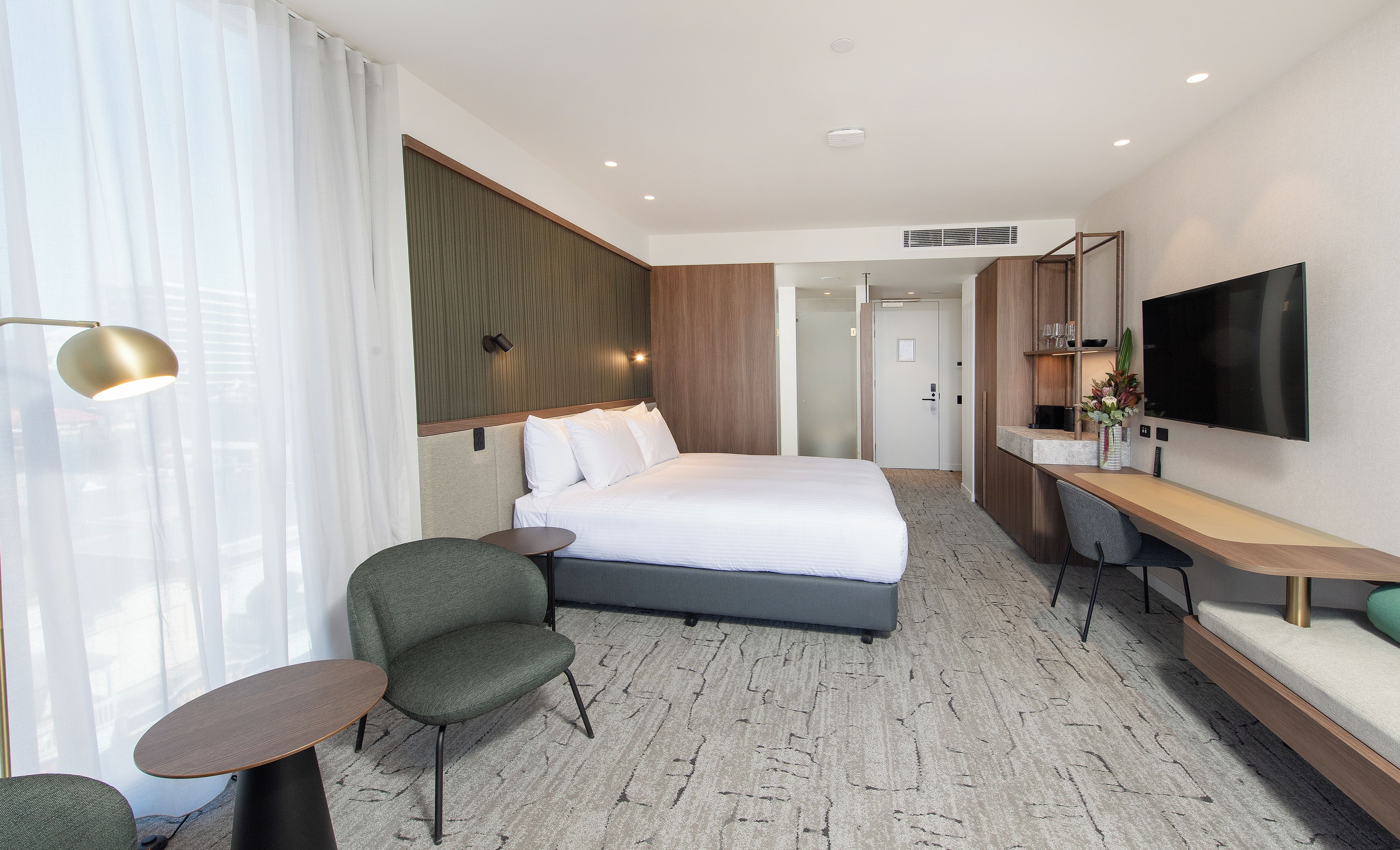 Une chambre d’hôtel avec un lit, un bureau, une chaise, une télévision et une fenêtre avec des rideaux.