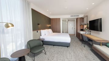 A hotel room with a bed, a desk, a chair, a TV, and a window with curtains.