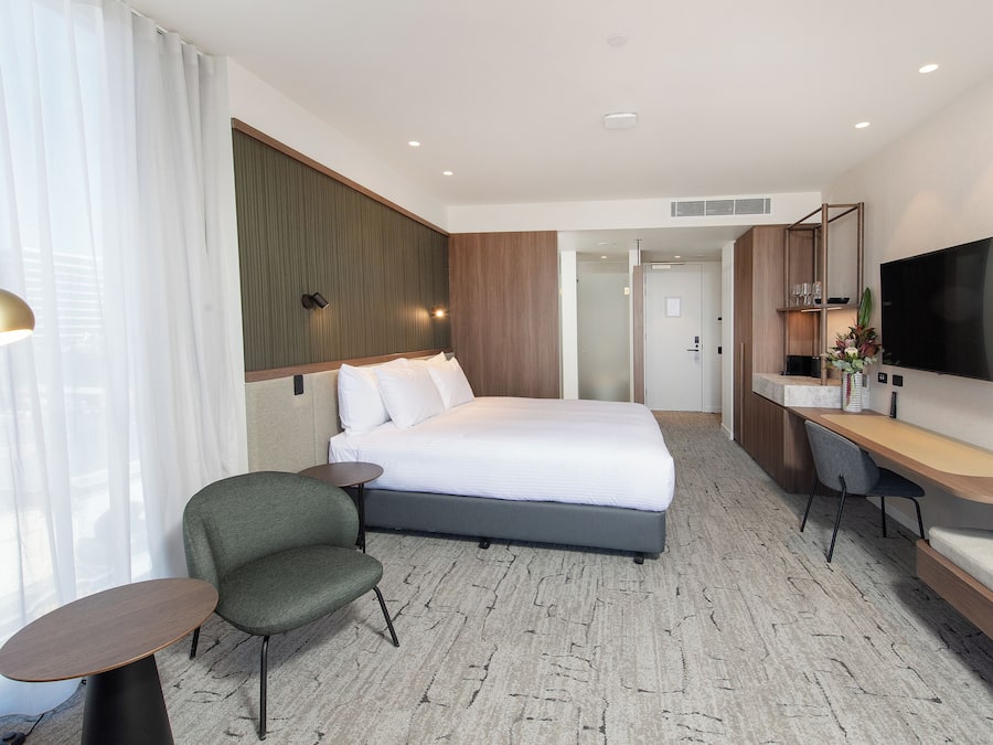 Una habitación de hotel con cama, escritorio, silla, televisión y ventana con cortinas.