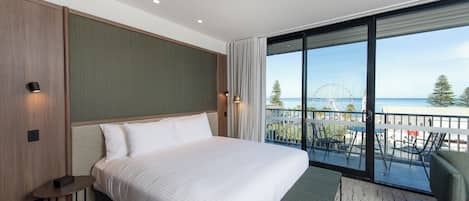 Et moderne hotelværelse med en stor seng, et lille bord og en balkon med udsigt til havet og et pariserhjul.