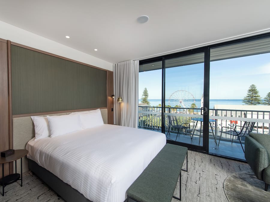 Habitación de hotel moderna con una cama grande, una mesita y un balcón con vistas al mar y una noria.