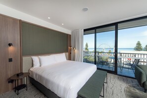Ein modernes Hotelzimmer mit einem großen Bett, einem kleinen Tisch und einem Balkon mit Blick auf das Meer und ein Riesenrad.