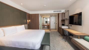 A modern hotel room with a large bed, a desk with a chair, a flat-screen TV, and a bathroom visible through an open door.
