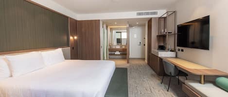 Una habitación de hotel moderna con una cama grande, un escritorio con silla, un televisor de pantalla plana y un baño visible a través de una puerta abierta.