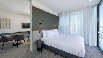 A modern hotel room with a large bed, a desk, a chair, and a television on the wall.