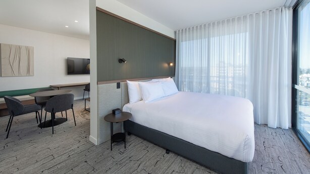 A modern hotel room with a large bed, a desk, a chair, and a television on the wall. - The George Glenelg (Adelaide)