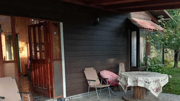 A covered outdoor area with a stone floor, a wooden table with a tablecloth, and two chairs. - Isla de Pino Huacho (Villarrica)
