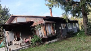 A rustic cabin with a sloped roof, a chimney, and a porch with outdoor furniture. - Isla de Pino Huacho (Villarrica)