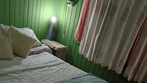 A bed with a blue blanket, a bedside table, and a green wall with a power outlet. - Isla de Pino Huacho (Villarrica)