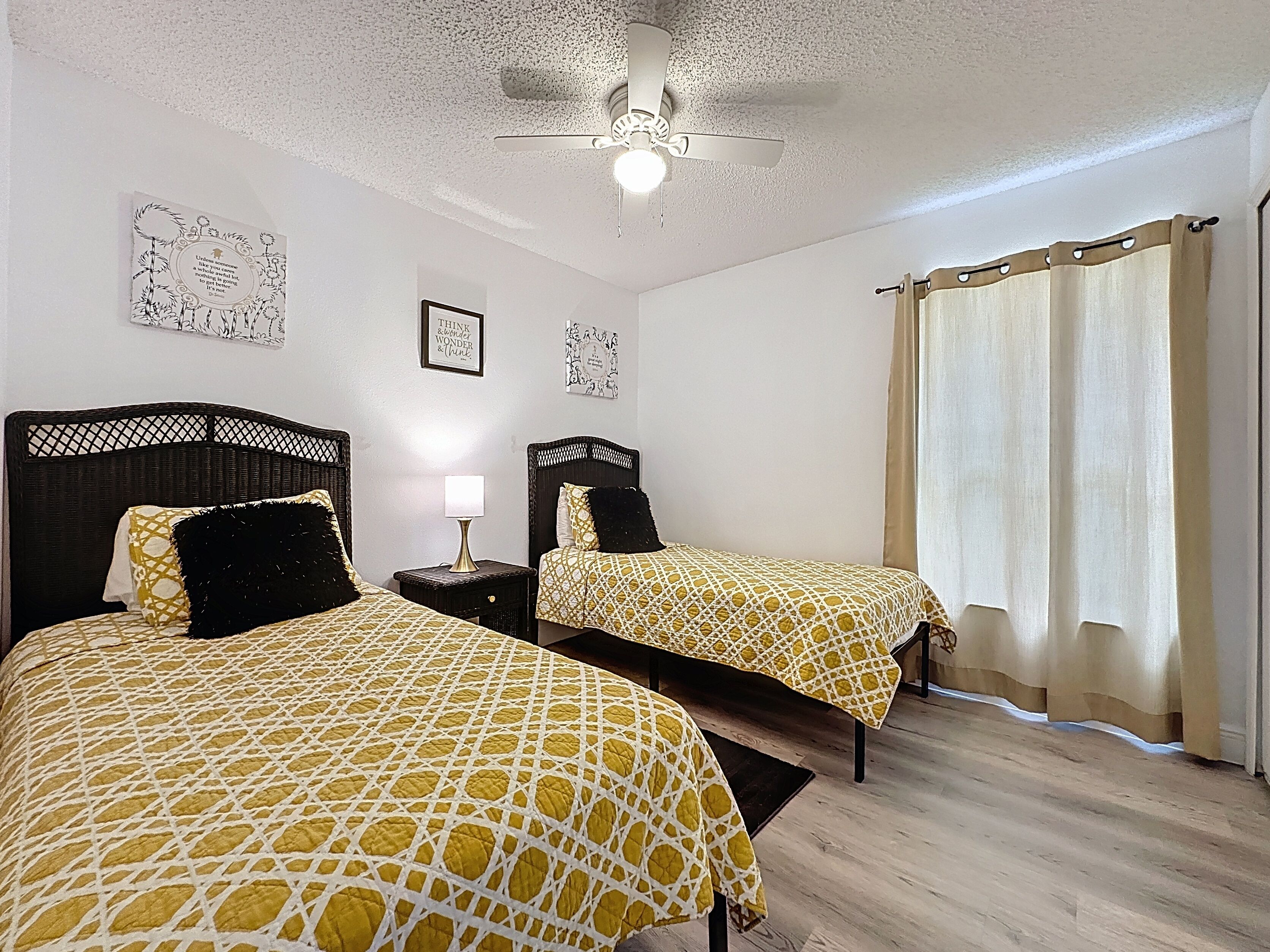 Ein Zimmer mit zwei Betten, einem Deckenventilator und einem Fenster mit Vorhängen.