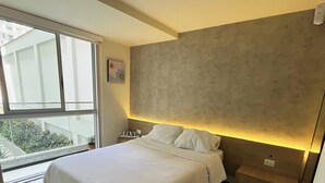 A modern bedroom with a large bed, a view of greenery outside, and a textured wall. - Coastal Blvd Apartment -Barranco (Lima)