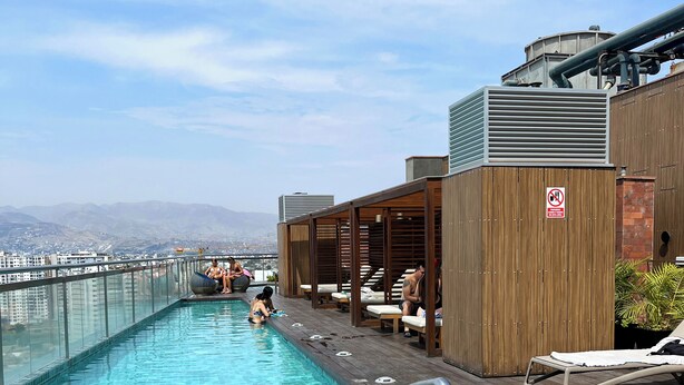 A rooftop pool with clear blue water, wooden deck, and lounge chairs. - Coastal Blvd Apartment -Barranco (Lima)