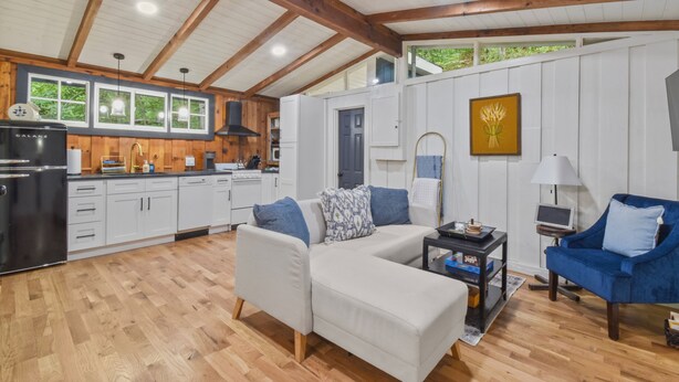 A spacious living area with a white sofa, blue armchair, and a kitchen with white cabinets and wooden beams. - Riverbend Retreat (Berryville)