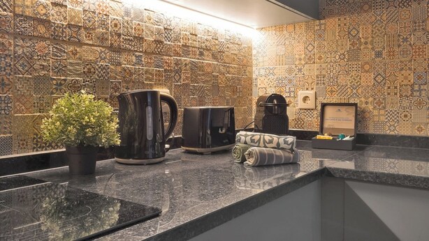 Una cucina moderna con schienale piastrellato con motivo, una macchina per il caffè, un bollitore e una piccola pianta in vaso.