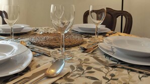 Un tavolo da pranzo apparecchiato con piatti bianchi, posate e bicchieri di vetro trasparenti, con un sottopiatti intrecciato al centro.