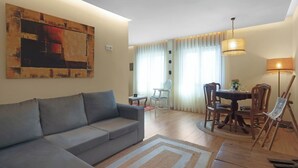 Un soggiorno con un divano grigio, un tavolo da pranzo con sedie, un quadro appeso e una lampada.