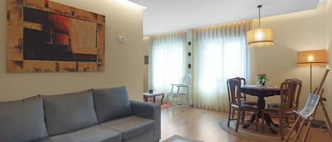 Un saló amb un sofà gris, una taula de dinar amb caires, un quadre a la paret i una làmpada.