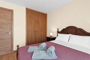 A bedroom with a wooden wardrobe, a bed with white linens, and a nightstand with a lamp. - Vintage Copio Apartment by MP (Vila Nova de Gaia)