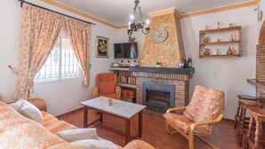 A living room with a fireplace, a sofa, a chair, a table, and a bookshelf. - Alabarce Nerja by Ruralidays (Málaga)