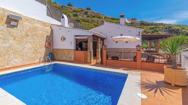 Une piscine avec un mur en pierre et un espace patio aménagé avec du mobilier d’extérieur.