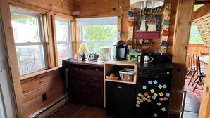 A compact kitchen with wooden cabinets, a refrigerator, a coffee maker, and a window with a view of greenery outside.