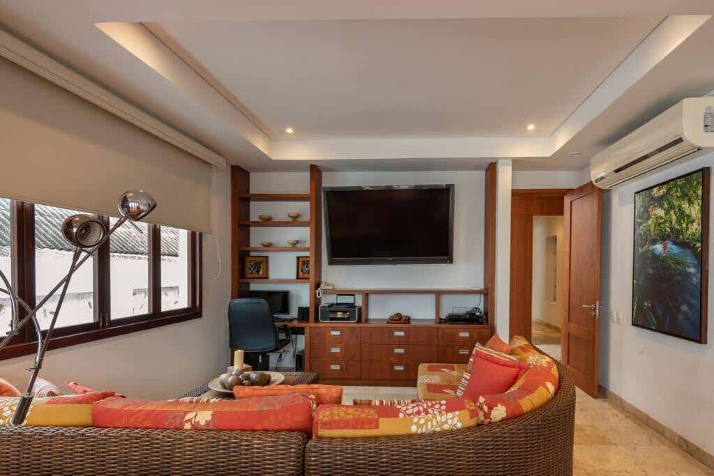 Un salón moderno con un televisor de pantalla plana grande, muebles de mimbre y un armario de madera.