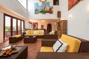 A spacious living area with wicker furniture, a large window, and a cityscape painting.