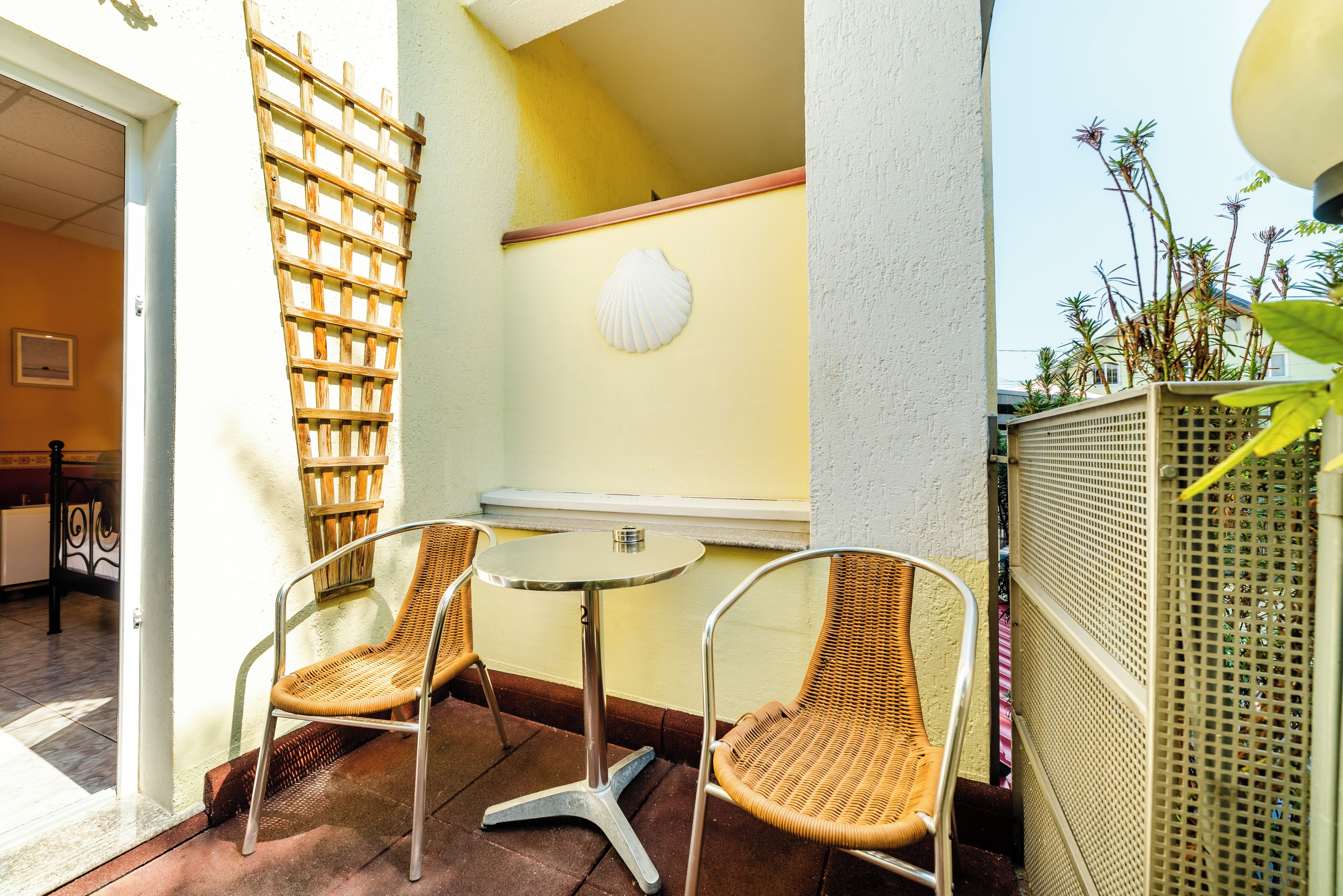 A small outdoor seating area with wicker chairs and a round table, a wooden lattice, and a white shell decoration on the wall.
