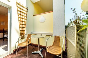 A small outdoor seating area with wicker chairs and a round table, a wooden lattice, and a white shell decoration on the wall.