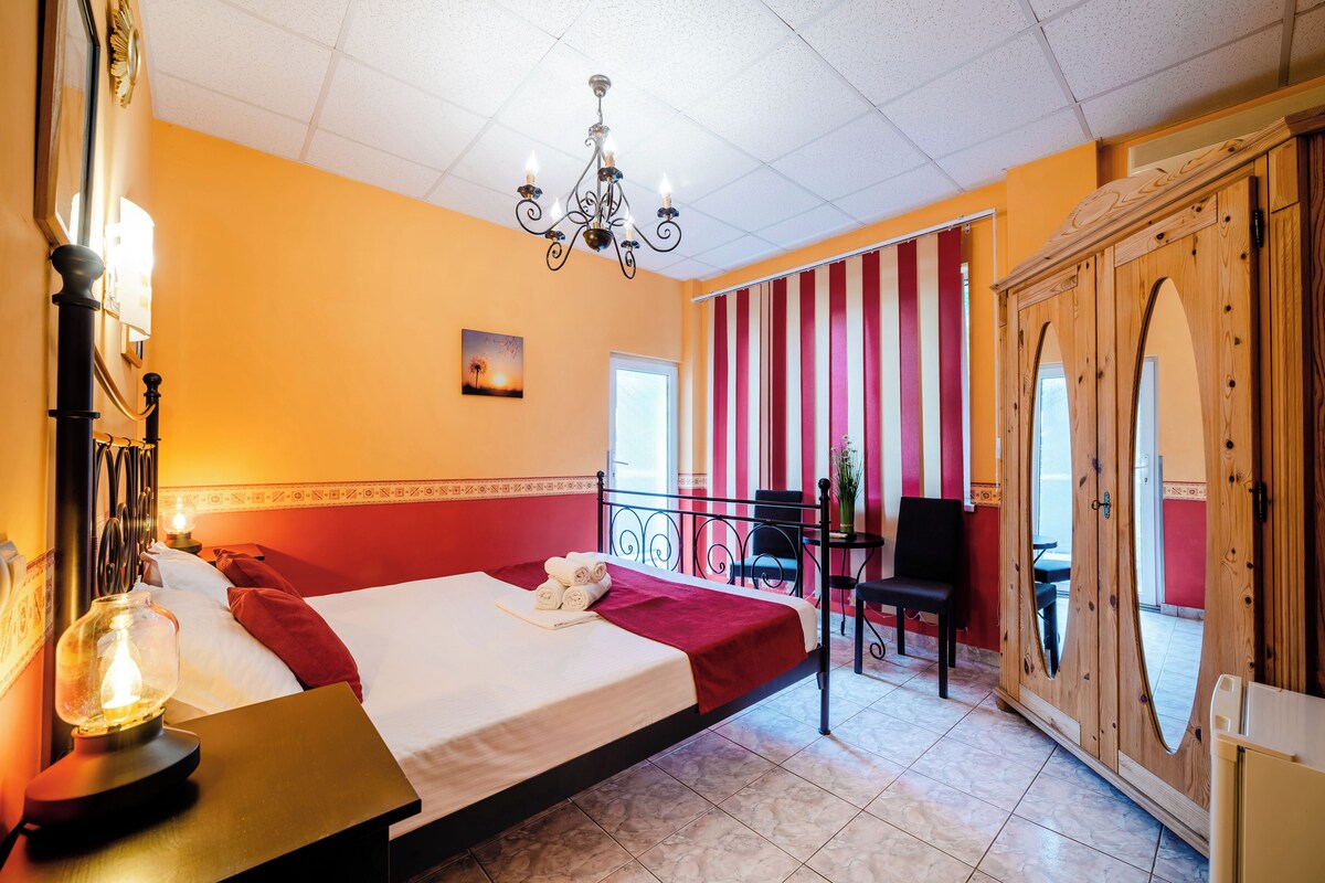 Habitación de hotel con cama, candelabro, armario de madera y vistas al balcón exterior.