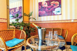 A dining area with wicker chairs, a glass table, a bottle of champagne, and two glasses.