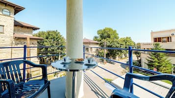 A balcony with a table, chairs, and a view of a street and buildings.