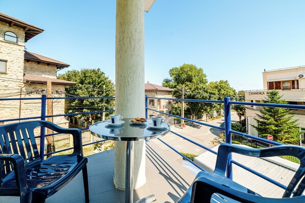 A balcony with a table, chairs, and a view of a street and buildings.