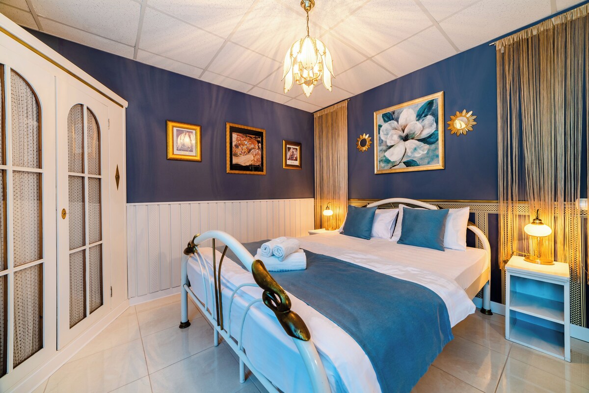 A hotel room with a large bed, a chandelier, and framed artwork on the walls.