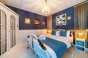 A hotel room with a large bed, a chandelier, and framed artwork on the walls.