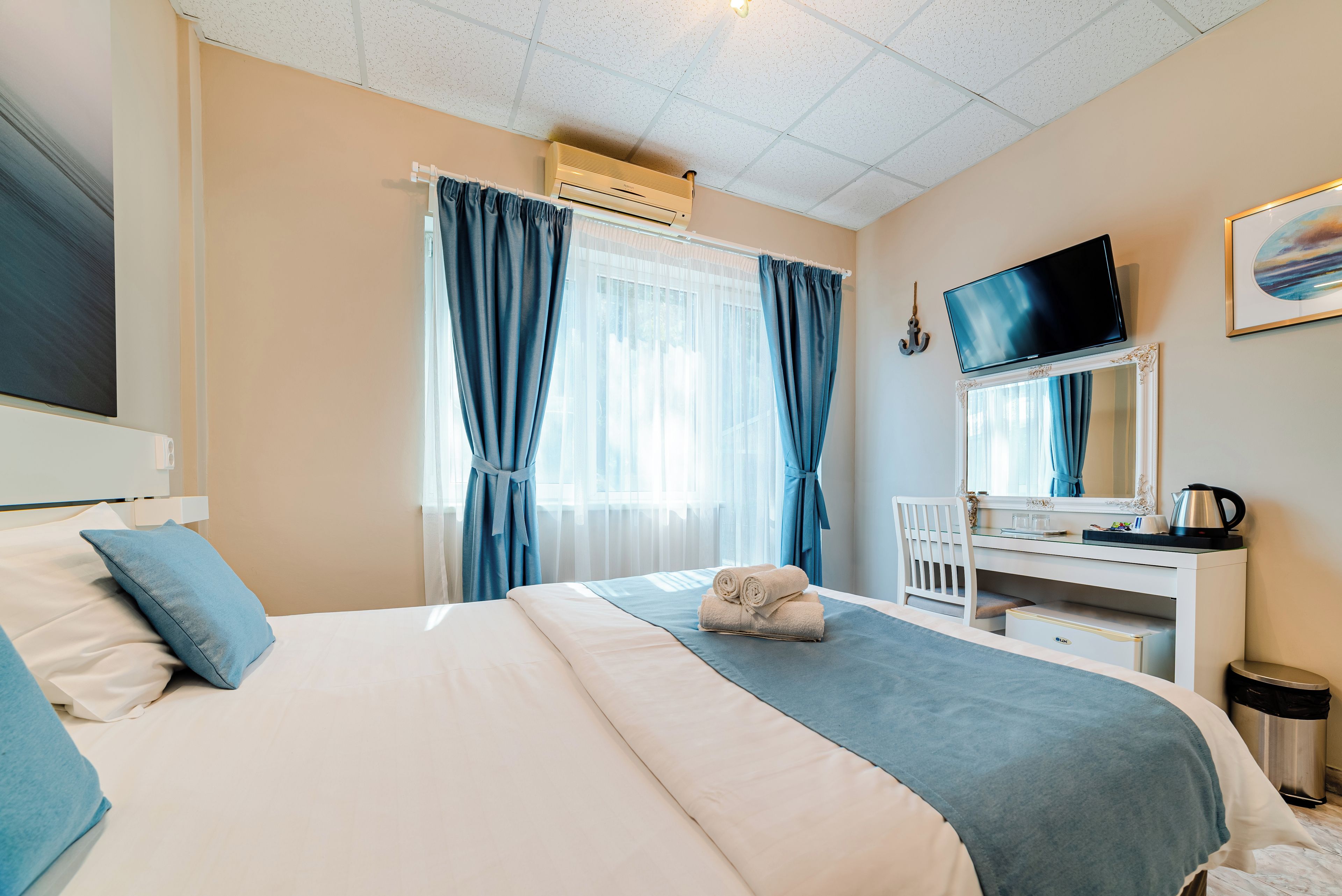 Ein Hotelzimmer mit einem Bett, einem Schreibtisch, einem Fernseher und einem Fenster mit Vorhängen.