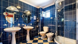 Une salle de bain avec des carreaux bleus, deux lavabos, des toilettes et une douche.