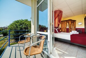 A balcony with wicker chairs and a table, a bed with a canopy, and a view of greenery.